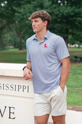 A young man wearing a blue and white striped polo shirt with a red logo on the chest, paired with off-white shorts, standing outdoors next to a stone wall with 'MISSISSIPPI' visible.