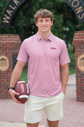 A young man stands outdoors holding a football, wearing a pink and white striped polo shirt with a small embroidered logo on the chest, paired with cream shorts.