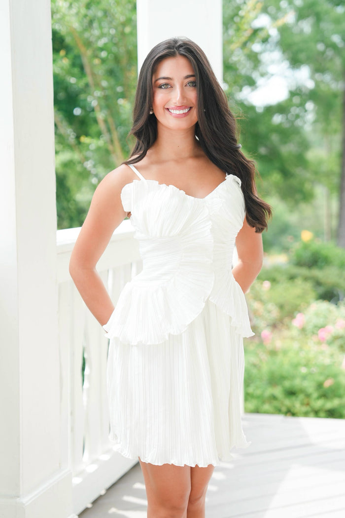 Woman in a white dress standing outdoors with greenery in the background