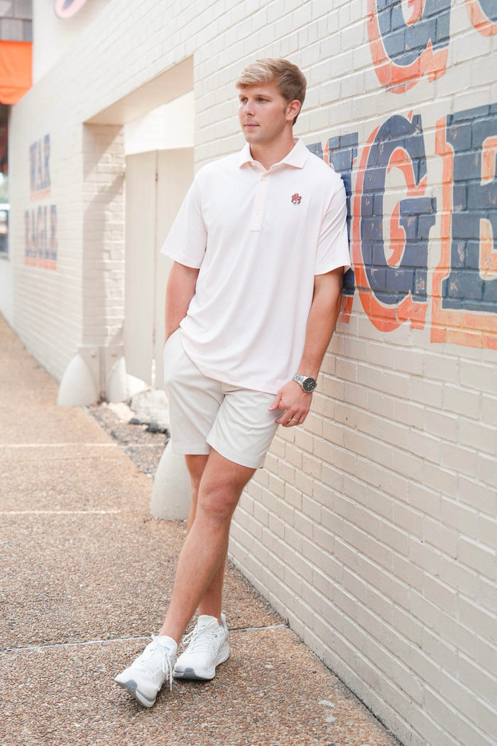 A man wearing a white short-sleeve polo shirt, white shorts, and white sneakers stands against a white brick wall with large painted letters.