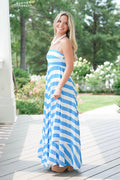 Woman in a blue and white striped dress standing on a wooden deck with greenery in the background